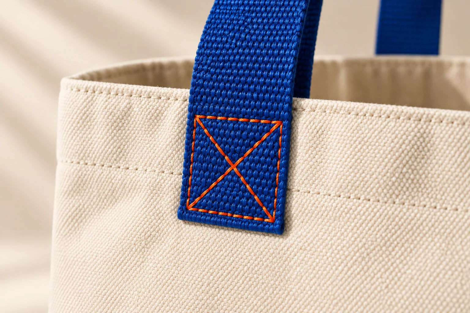 AI concept close-up of blue webbing and orange reinforcement stitching on an ivory canvas-look tote